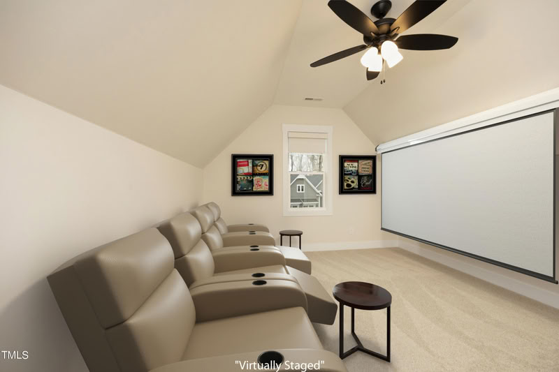 Home theater with sloped ceiling, beige carpet, leather recliners, and a large projector screen. A window provides natural light.