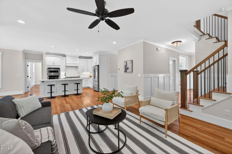 Open-plan living space with hardwood floors, a modern white kitchen with an island, and a staircase with a wood and metal railing.