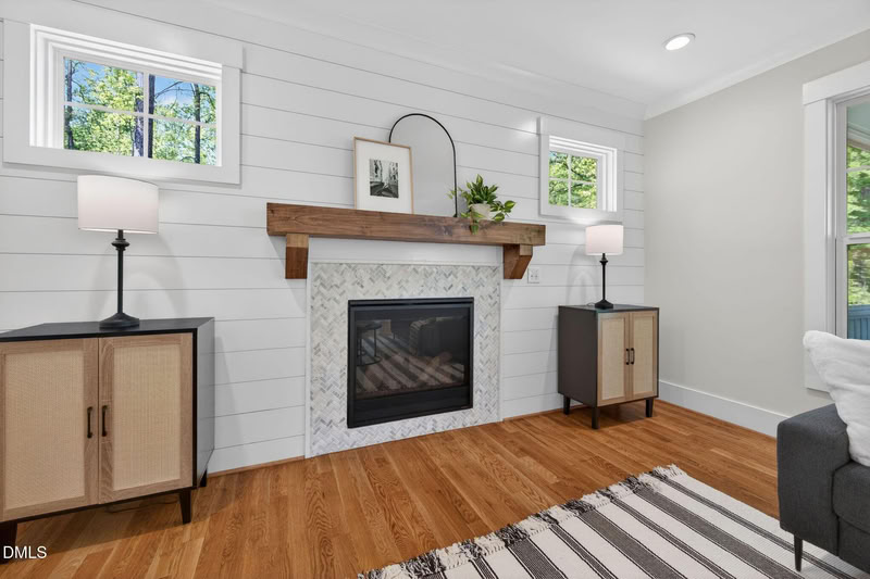 Living room with a shiplap wall, a fireplace with herringbone tile and a wood mantel, flanked by windows and cabinets.