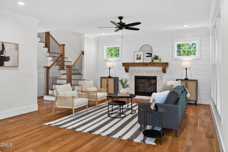 Bright living room with hardwood floors, a shiplap accent wall with a tiled fireplace, modern furniture, and a wooden staircase.