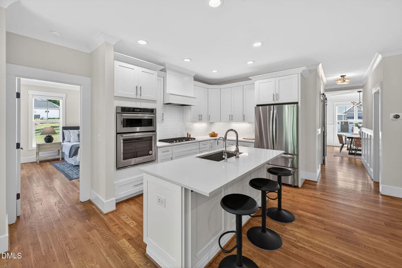 Bright kitchen with white shaker cabinets, quartz countertops, stainless appliances, and a center island on hardwood floors.