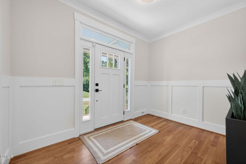 A bright entryway with hardwood floors, white wainscoting, and a white front door with glass panes, sidelights, and a transom window.