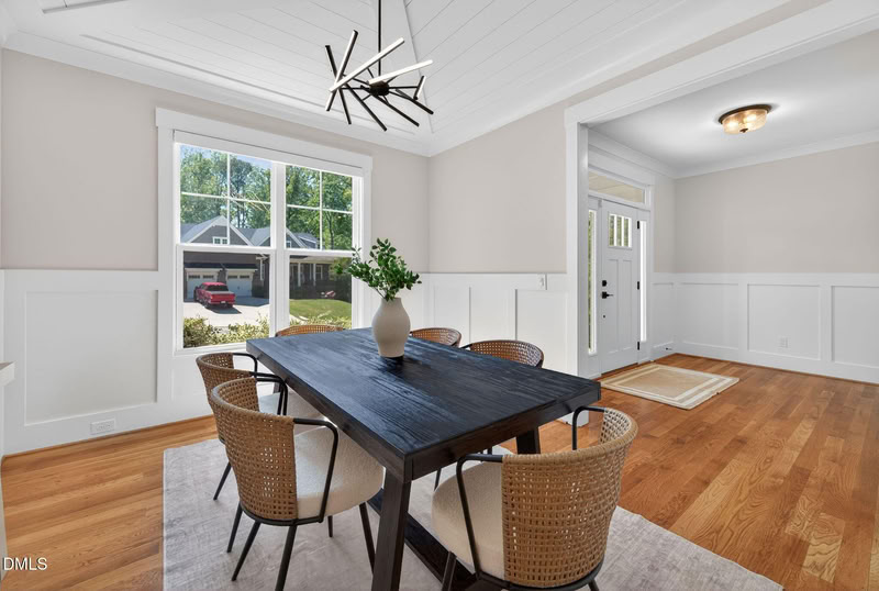 Dining room with hardwood floors, white wainscoting, a modern chandelier, and a large window providing natural light.