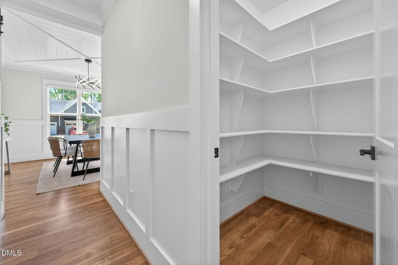 Hallway with white wainscoting and an open door revealing a large walk-in pantry with extensive built-in shelving.