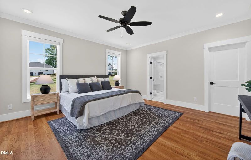Spacious primary bedroom with hardwood floors, natural light from two windows, and a door leading to an en-suite bathroom.