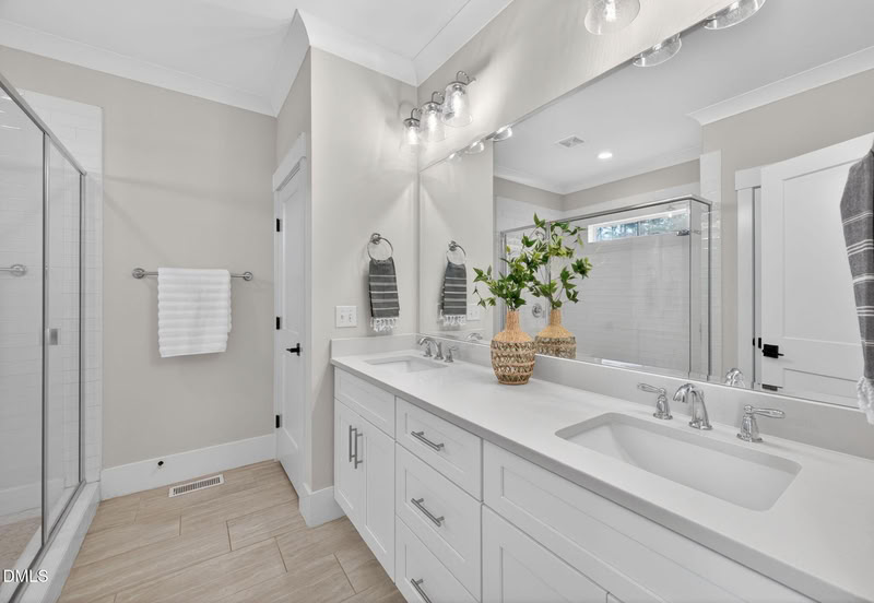 Bright bathroom with a white double vanity, quartz countertop, large mirror, and a glass-enclosed tiled shower.