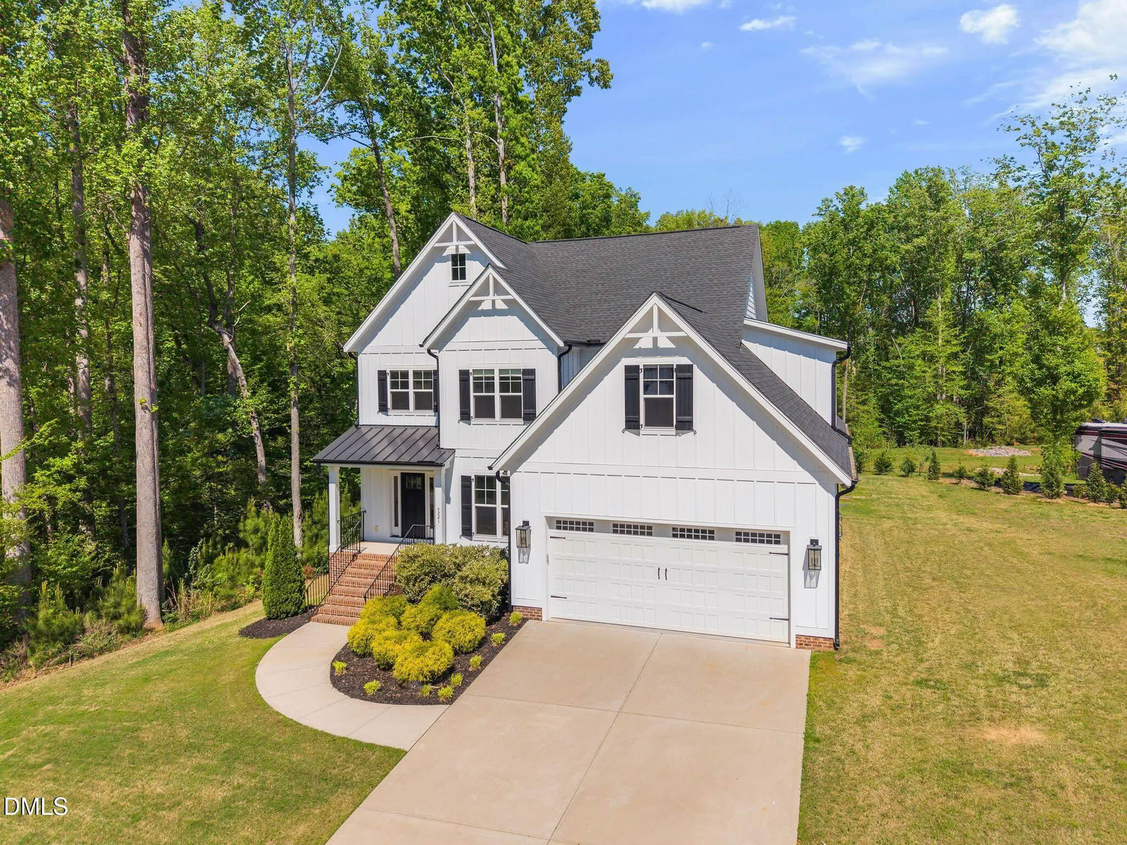 A white modern farmhouse with multiple gables, black shutters, and a two-car garage, nestled in a wooded lot on a sunny day.