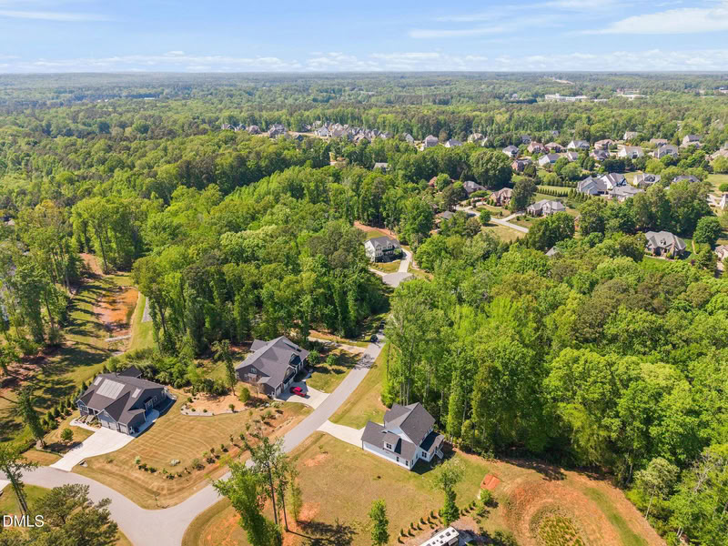 Aerial view of a sprawling, wooded neighborhood with large homes on spacious lots under a clear blue sky.