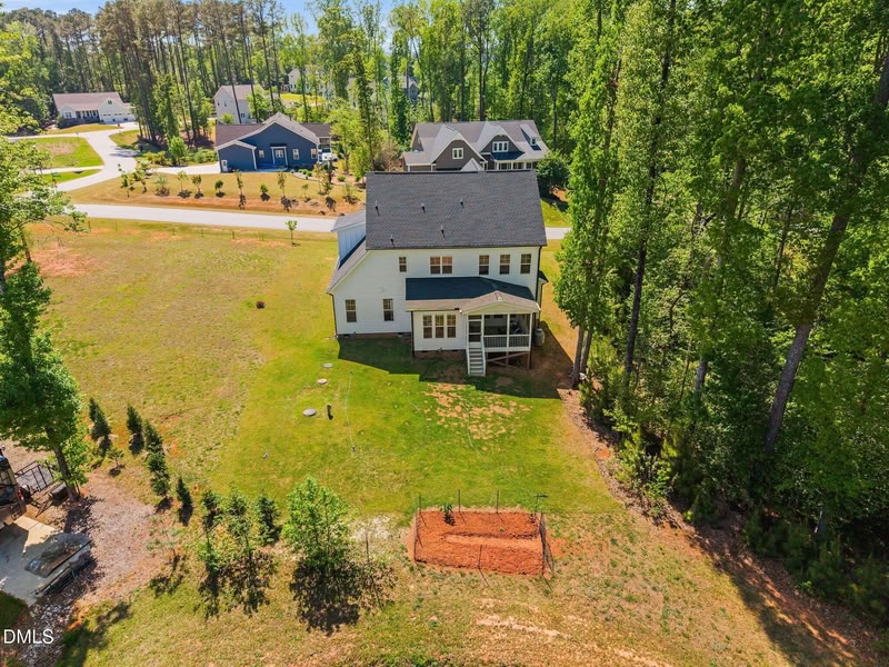 Aerial view of a white two-story house with a large, grassy backyard, screened porch, and a border of mature trees.